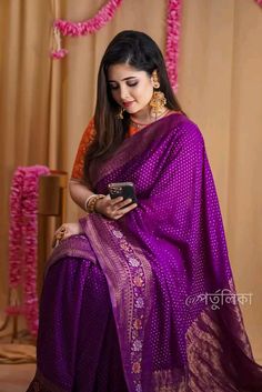 a woman in a purple sari is holding a cell phone and looking at it