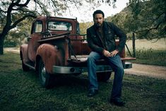 a man sitting on the back of an old pickup truck in front of a tree