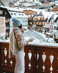 a woman standing on top of a balcony next to snow covered buildings