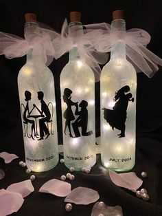 three lighted bottles with silhouettes of people sitting at a table on top of petals