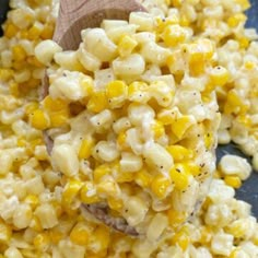 a wooden spoon filled with corn on top of a blue plate and another bowl in the background