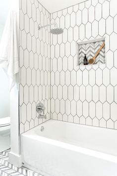 a white tiled bathroom with hexagonal tiles on the shower wall and bathtub