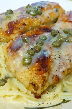 two pieces of chicken with green peas on top of pasta