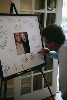 a man writing on a large white board with pictures and autographs attached to it