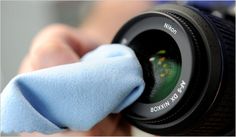 a person holding a camera lens with a blue cloth on it's thumb and cleaning the lens