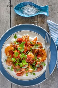 a white plate topped with shrimp and garnish next to a blue bowl filled with rice