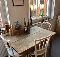 a wooden table with chairs and bottles on top of it in front of a window