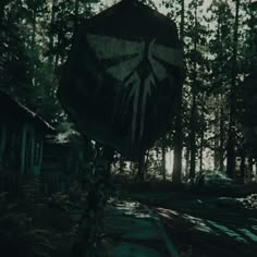 a creepy looking umbrella in the middle of a dark forest with trees and houses behind it