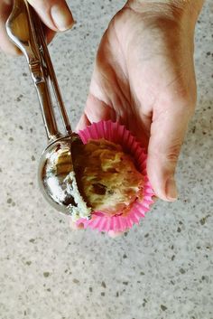 a hand holding a spoon with a muffin in it on top of a pink cupcake liner