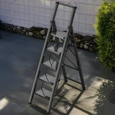 a metal step ladder sitting on top of a cement floor next to a bush and building