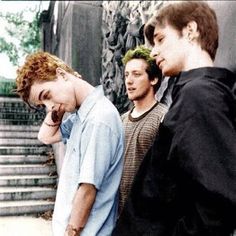 three young men standing next to each other talking on their cell phones in front of some stairs