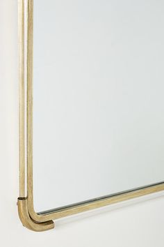 a mirror hanging on the wall with a gold frame and metal bar around it's edge