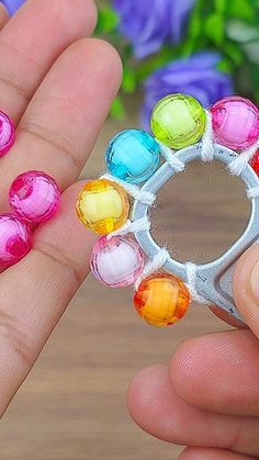 a hand holding a colorful ring made out of plastic beads with flowers in the background