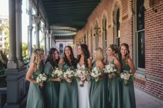 a group of women standing next to each other in front of a brick building holding bouquets