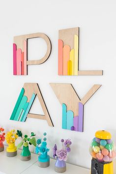 colorful wooden letters and vases on a white shelf next to a wall with flowers