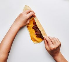 two hands reaching for a hot dog bun with mustard and ketchup on it