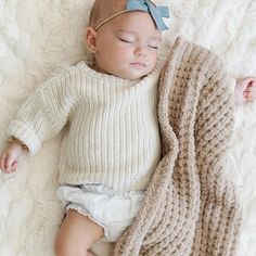 a baby is sleeping with a blanket on top of it's head and wearing a blue bow