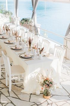 a table set up with white chairs and flowers