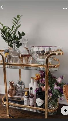 a gold bar cart filled with bottles and glasses on top of a hard wood floor