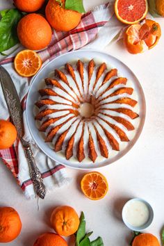 an orange bundt cake with icing on a plate surrounded by sliced oranges