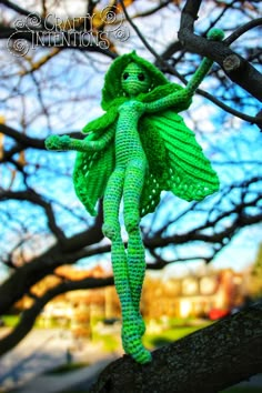 a green knitted doll hanging from a tree branch