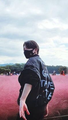 a person wearing a face mask standing in front of pink grass