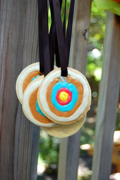 three cookies hanging from a black ribbon on a wooden fence with trees in the background