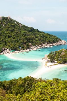 an island with white sand and blue water surrounded by green trees in the foreground