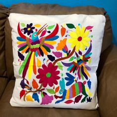 a colorful embroidered pillow sitting on top of a brown couch