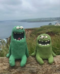 two green stuffed animals sitting on top of a wooden log next to each other with their mouths open