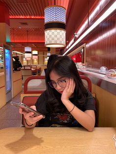 a woman sitting at a table with a cell phone in her hand and looking at the screen