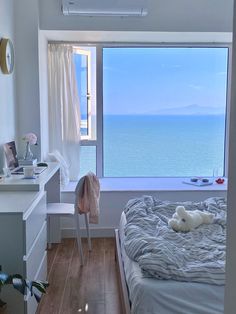 a bedroom with a bed, desk and window looking out to the ocean on a sunny day