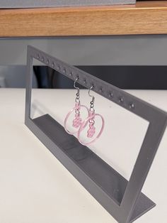 a pair of pink earrings hanging from a metal frame on a white counter top next to a computer keyboard