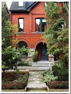 a red brick house with steps leading up to the front door and trees surrounding it