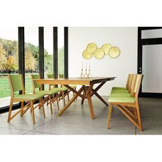 a dining room table with green chairs and plates on the wall next to it in front of large windows