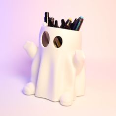 a white plastic container with pens and pencils in the shape of a ghost, on a pink background