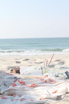 an open laptop computer sitting on top of a beach covered in blankets next to the ocean