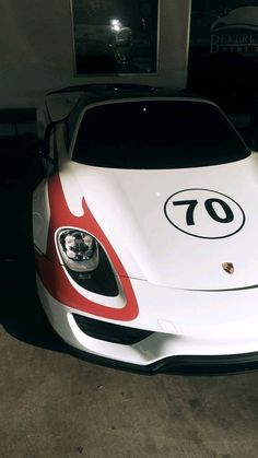 a white and red sports car parked in front of a garage door with the number 70 on it's side