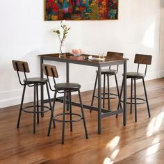 a kitchen table with four stools and a painting on the wall