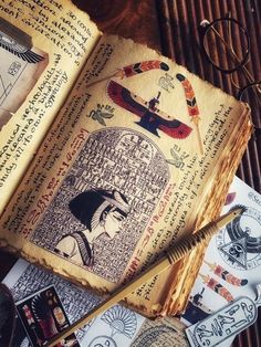 an open book sitting on top of a wooden table next to some writing utensils