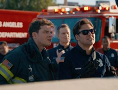 two firemen standing next to each other in front of a firetruck and some people