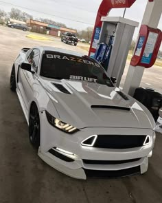 a white car is parked in front of a gas station with its hood up and lights on