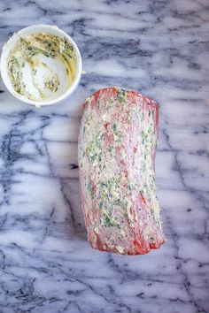 a piece of meat next to a bowl of dip on a marble counter top with other food items