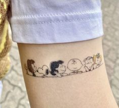 a person with a tattoo on their arm that has peanuts and friends drawn on it