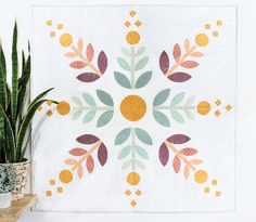 a potted plant sitting next to a white wall with a colorful quilt on it