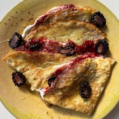 two crepes with berries and cream on a yellow plate