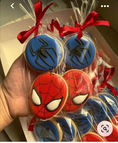 a person holding up some decorated cookies in plastic bags with red ribbon around them and spiderman faces on them