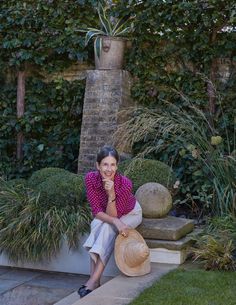 a woman is sitting on the steps in front of some bushes and plants with her hand under her chin