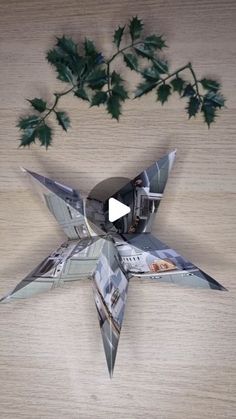 an origami bird made out of photos and leaves on a wooden table with a video playing below it