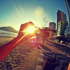 the sun is shining brightly over a beach with buildings in the background and a person holding their hand up to the camera